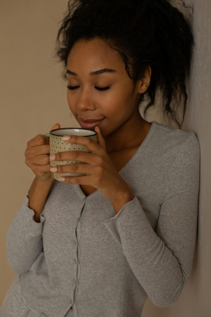 Young woman with eyes closed, enjoying a comforting hot drink against a neutral background.